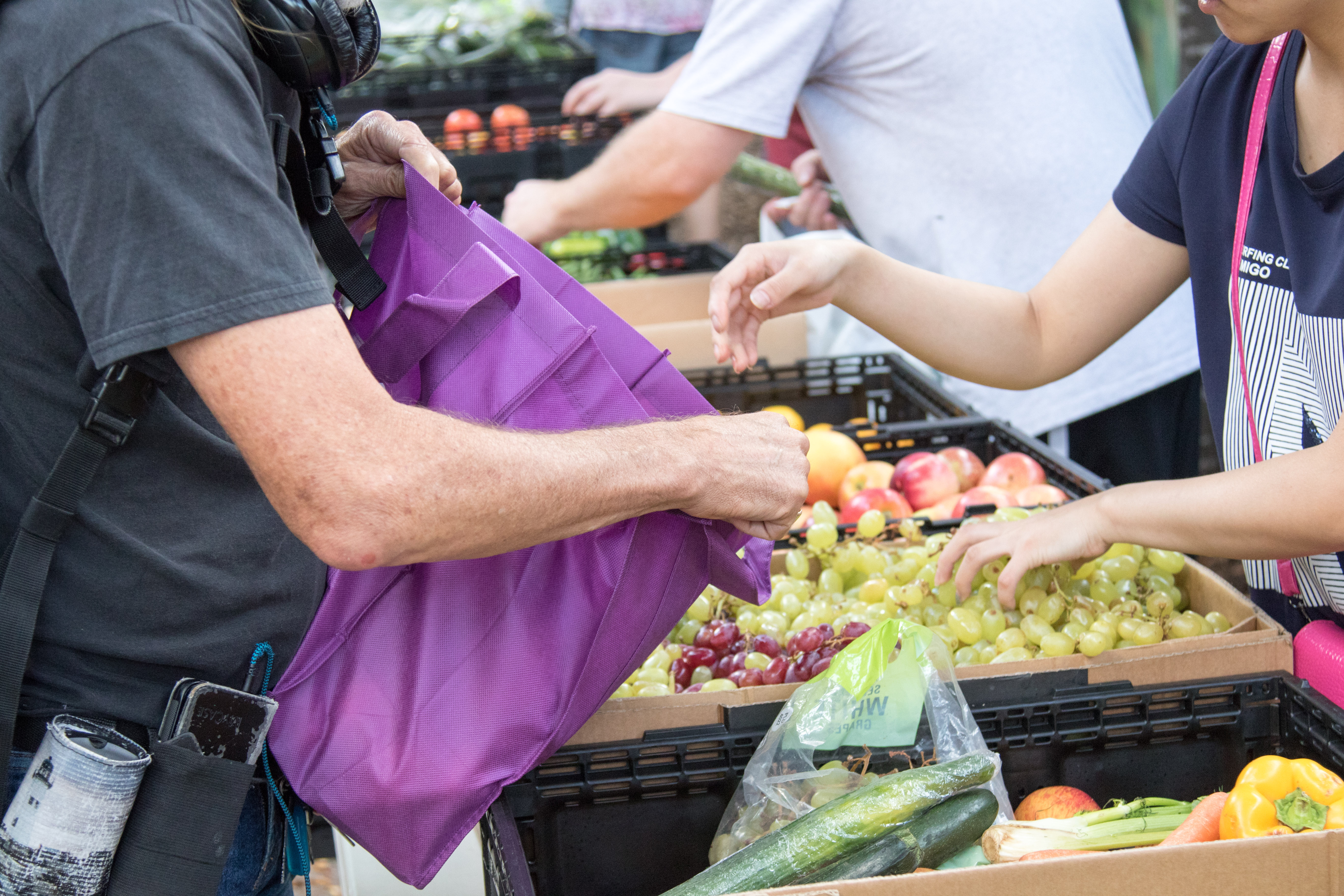 Person getting food from a market, carrying a purple bag.