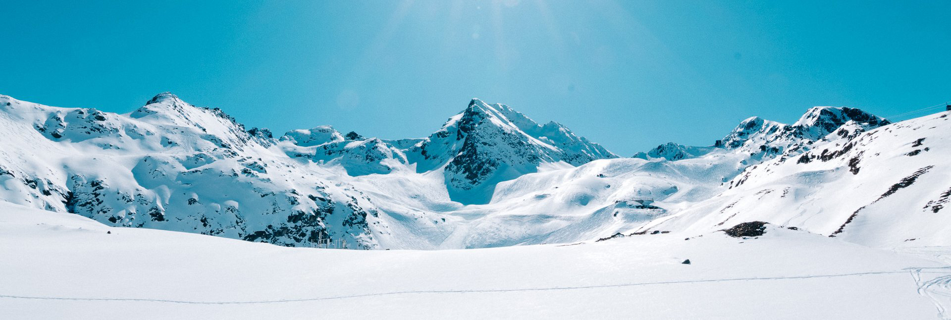 Eine Berglandschaft im Schnee, der Gipfel ist in der Mitte, dahinter blauer Himmel.