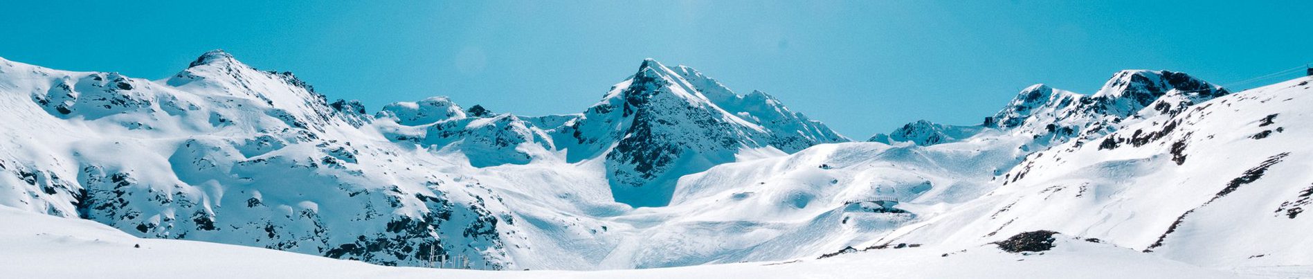 Berglandschaft im Schnee, Gipfel in der Mitte, hellblauer Himmel im Hintergrund.