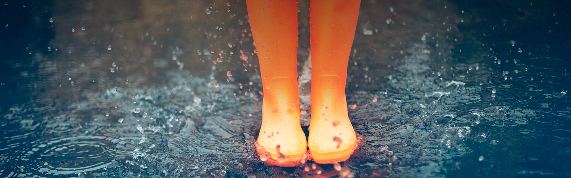 Allianz Partners Deutschland – Presse: Orange Gummistiefel spritzen in einer Pfütze, Wassertropfen und Wellen sind sichtbar.