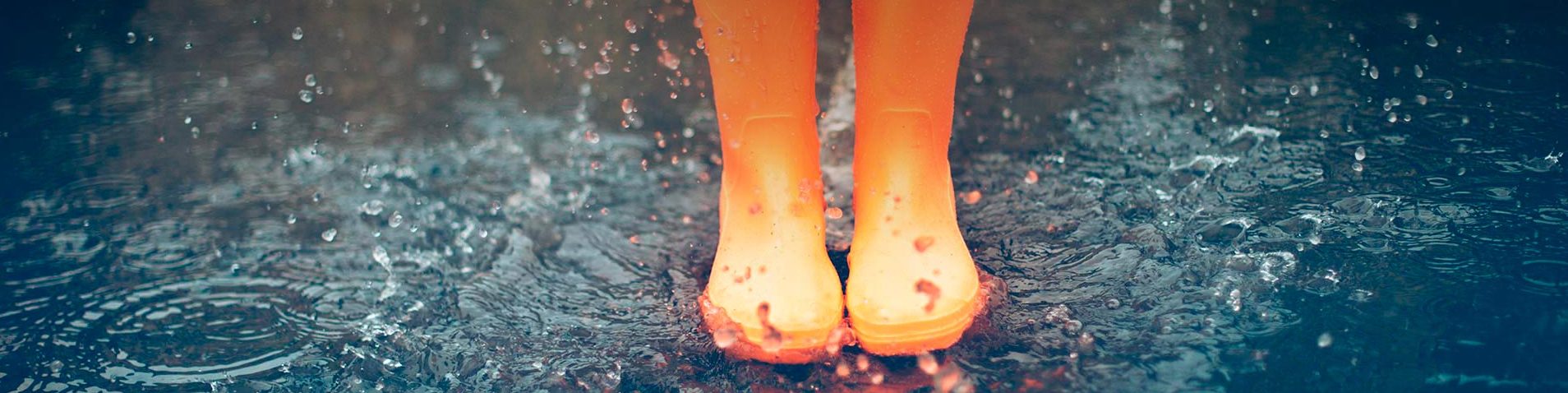 Allianz Partners Deutschland – Presse: Orange Gummistiefel spritzen in einer Pfütze, Wassertropfen und Wellen sind sichtbar.