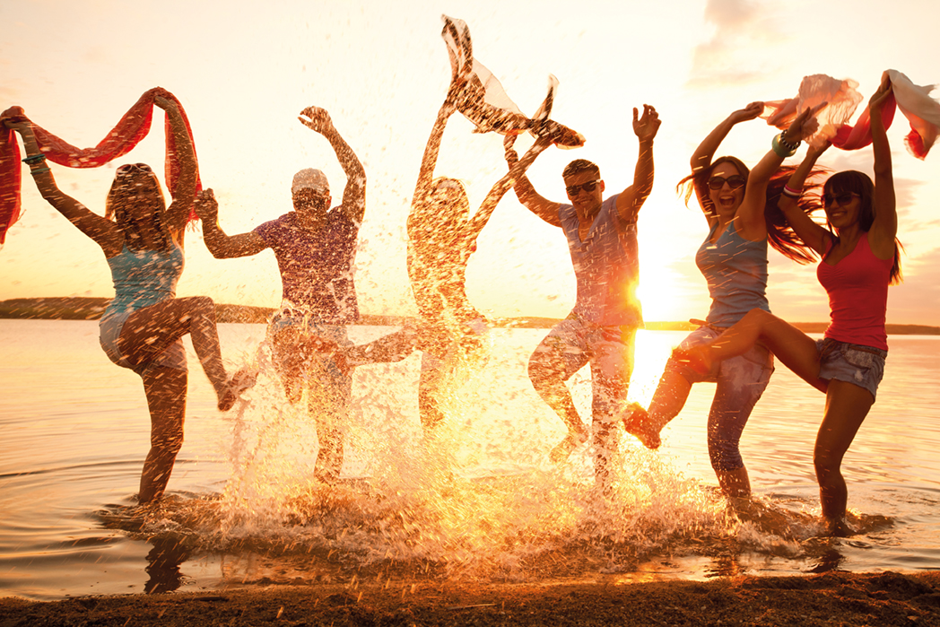 Eine Gruppe an Menschen tanzen im Wasser bei Sonnenuntergang.