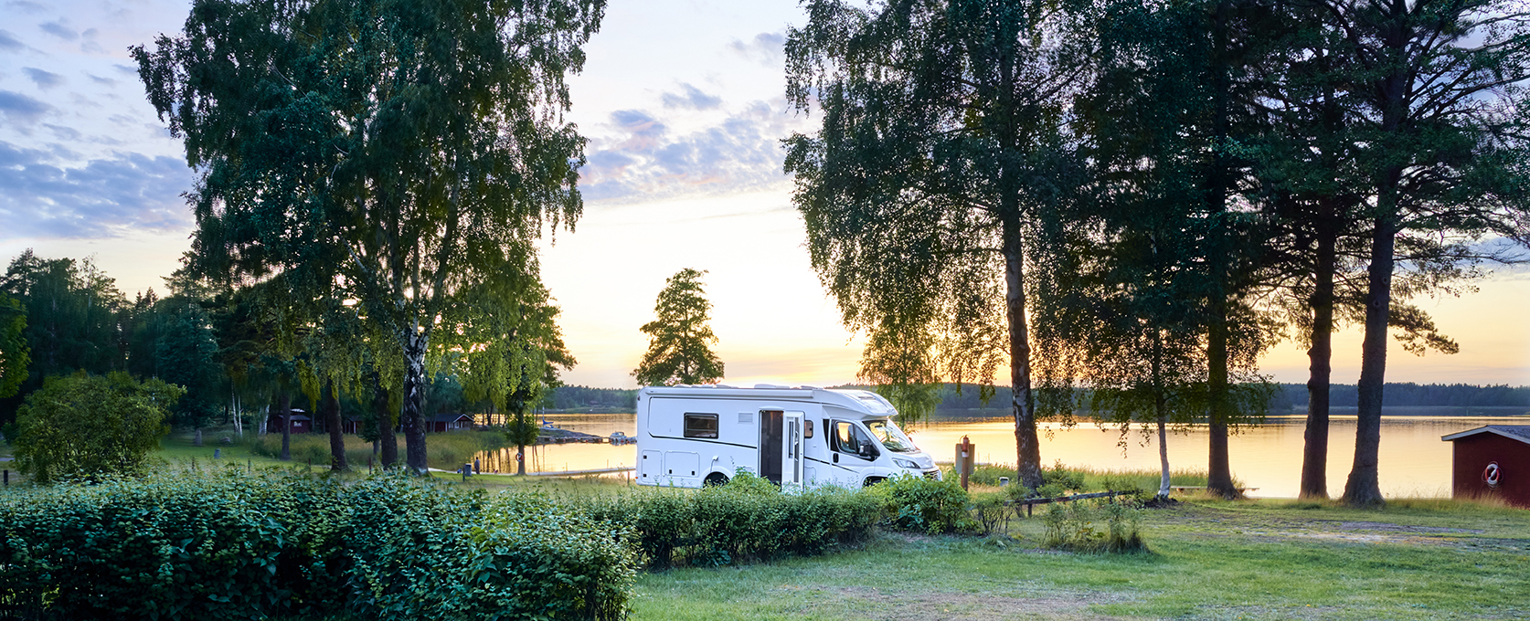 Ein weißes ohnmobil steht auf einer Wiese am See bei Sonnenuntergang.