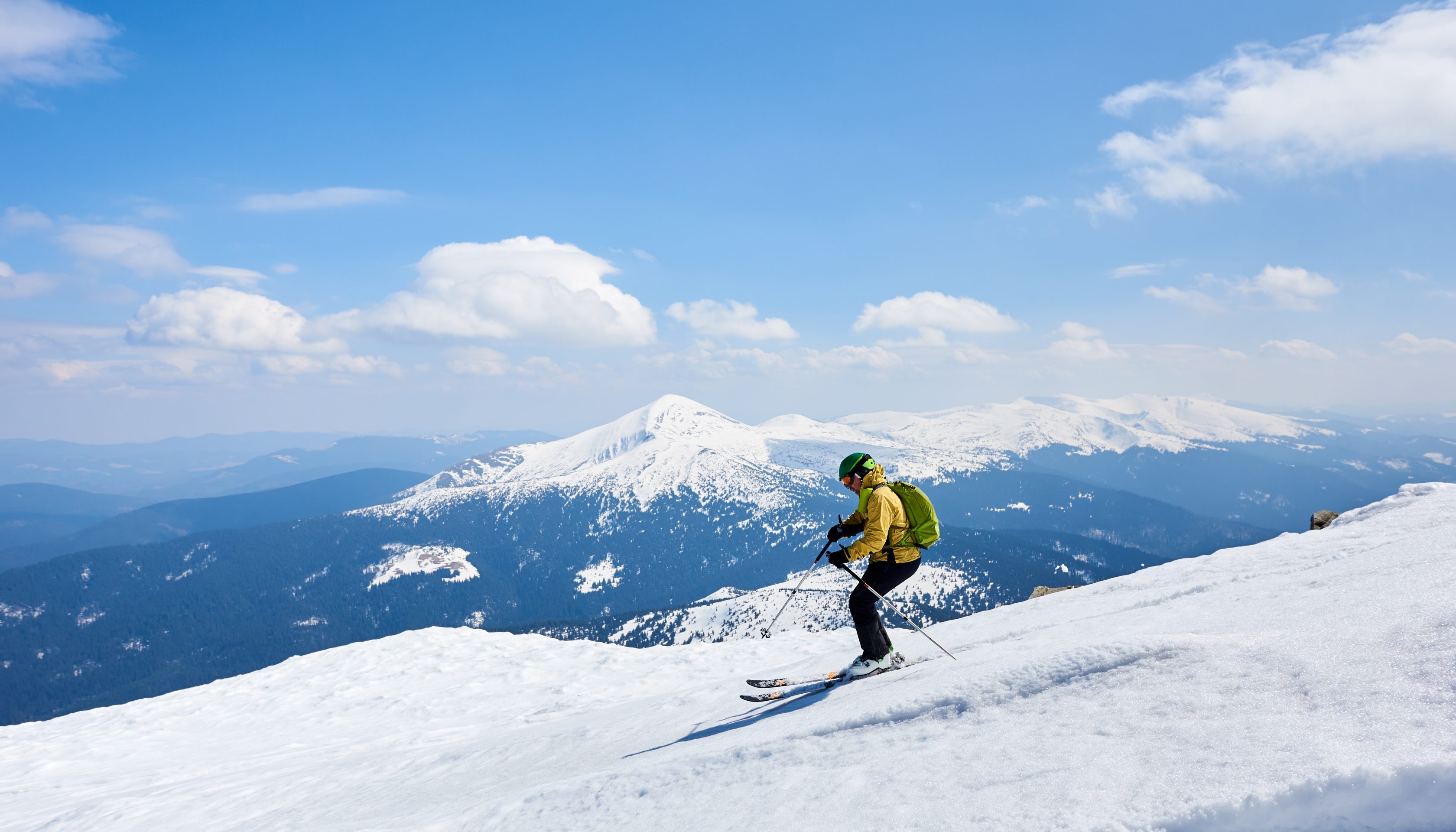 Allianz Partners Deutschland – Winterreise-Studie: Ein Skifahrer in gelber Jacke fährt eine Piste hinunter, umgeben von schneebedeckten Bergen.