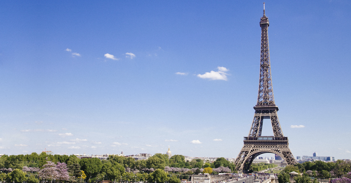 Der Eiffelturm unter blauem Himmel mit grünen Bäumen außen herum. 