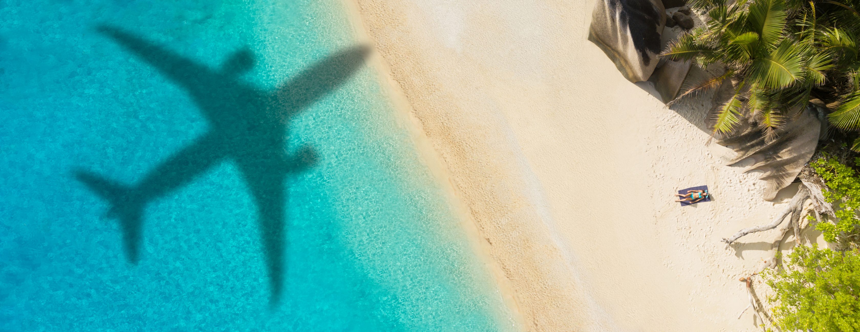 Tropischer Strand mit türkisfarbenem Wasser, weißem Sand, Palmen und einer Frau die sich im Bikini sonnt und einem Flugzeugschatten über der Oberfläche.