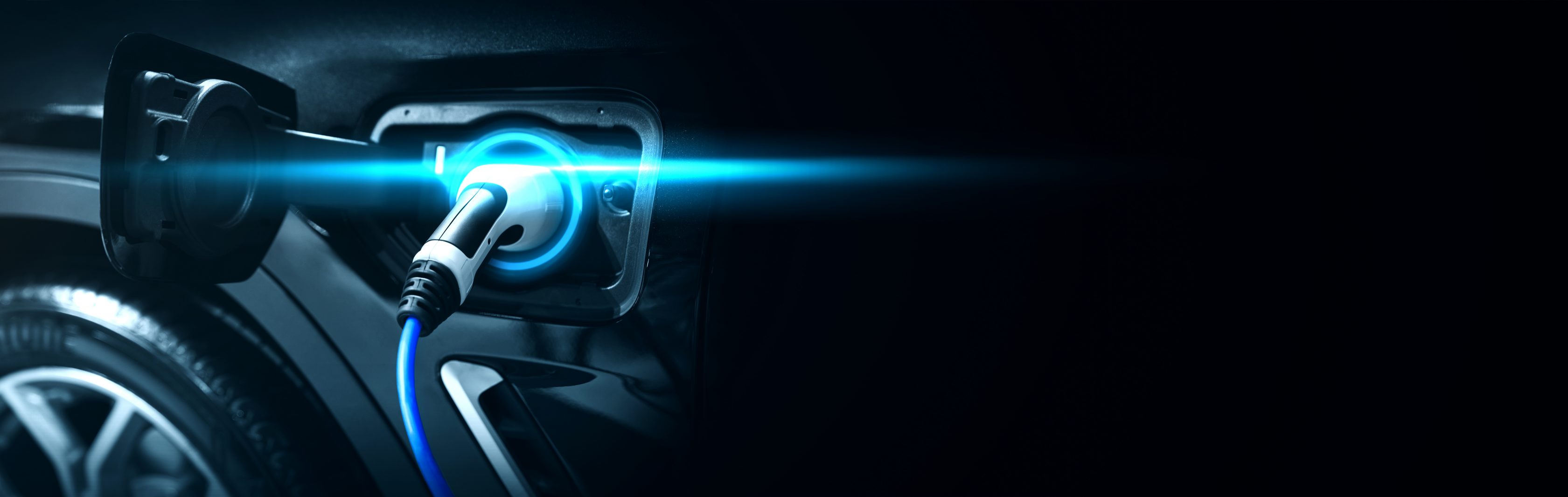 Nahaufnahme eines Elektrofahrzeug-Ladeanschlusses mit eingestecktem blauem Ladekabel, das ein blaues Licht ausstrahlt.