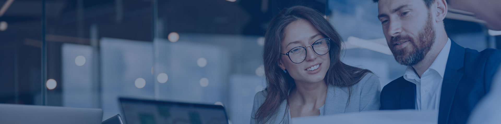 Ein Mann und einer Frau in professioneller Kleidung schauen auf ein Dokument in einem hellen Büroraum.