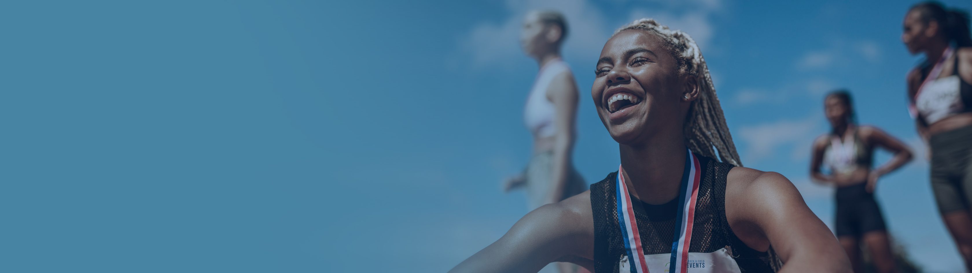 Allianz Partners Deutschland – Unterstützung für die Olympischen Spiele Paris 2024: Eine Athletin mit Medaille sistzt auf dem Boden und lacht. Im Hintergrund sind mehr Atheltinnen.