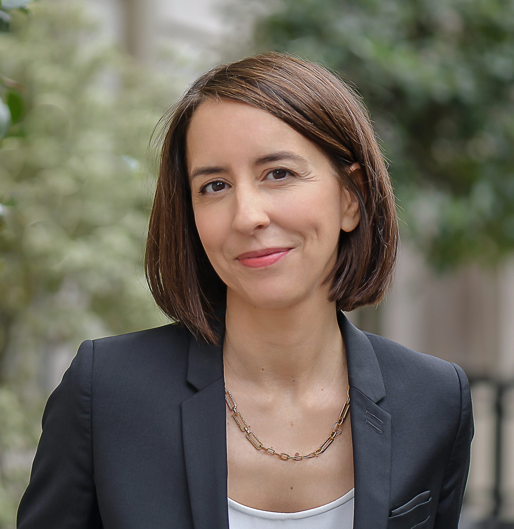Eine Frau mit kurzen braunen Haaren un in schwarzem Blazer lächelt in die Kamera.