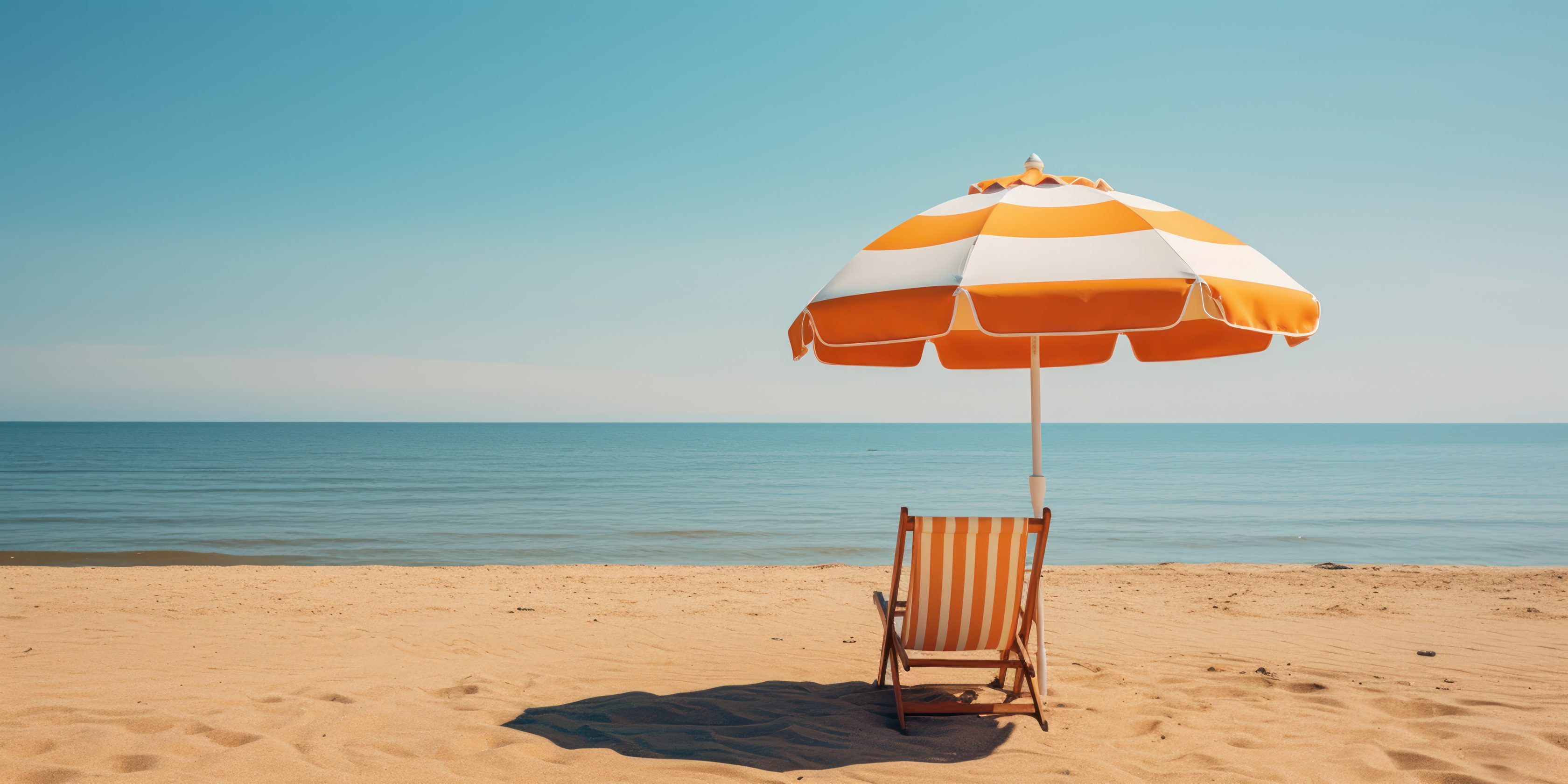 Eine weiß-gelb gestreifte Sonnenliege und ein Sonnenschirm sind an einem Sandstrand am Meer.