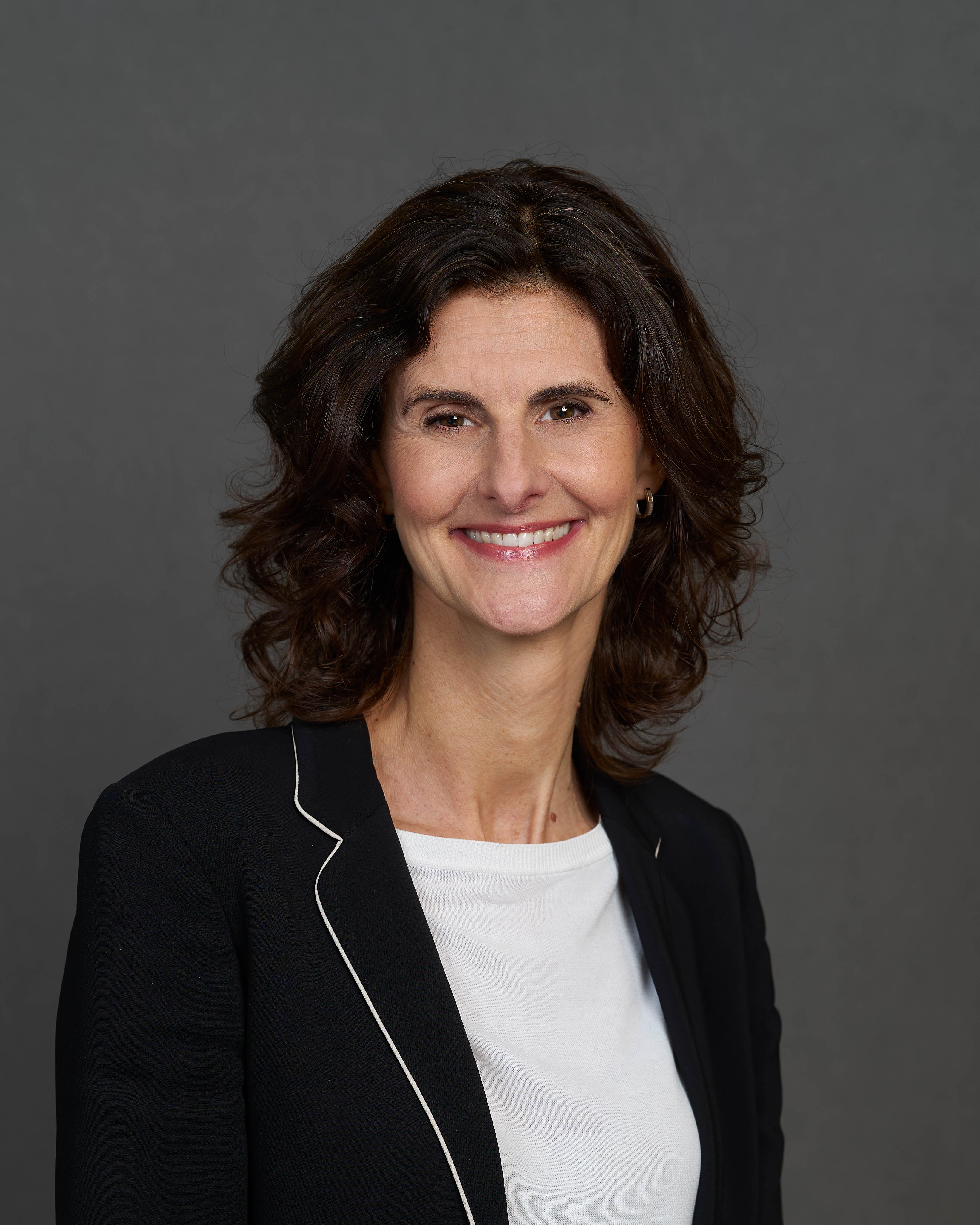 Porträt von Anna Kofoed, Chief Officer Global Strategic Partnerships bei Allianz Partners, eine Frau mit schulterlangem braunen Haar, schwarzem Blazer und weißem T-Shirt lächelt in die Kamera.