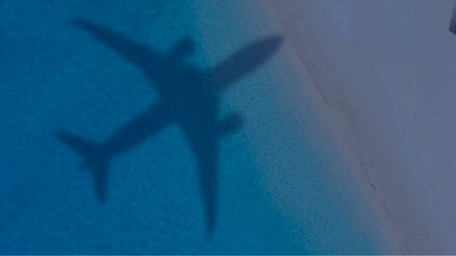 Ein Schatten eines Fliegers ist über dem Meer zu sehen.