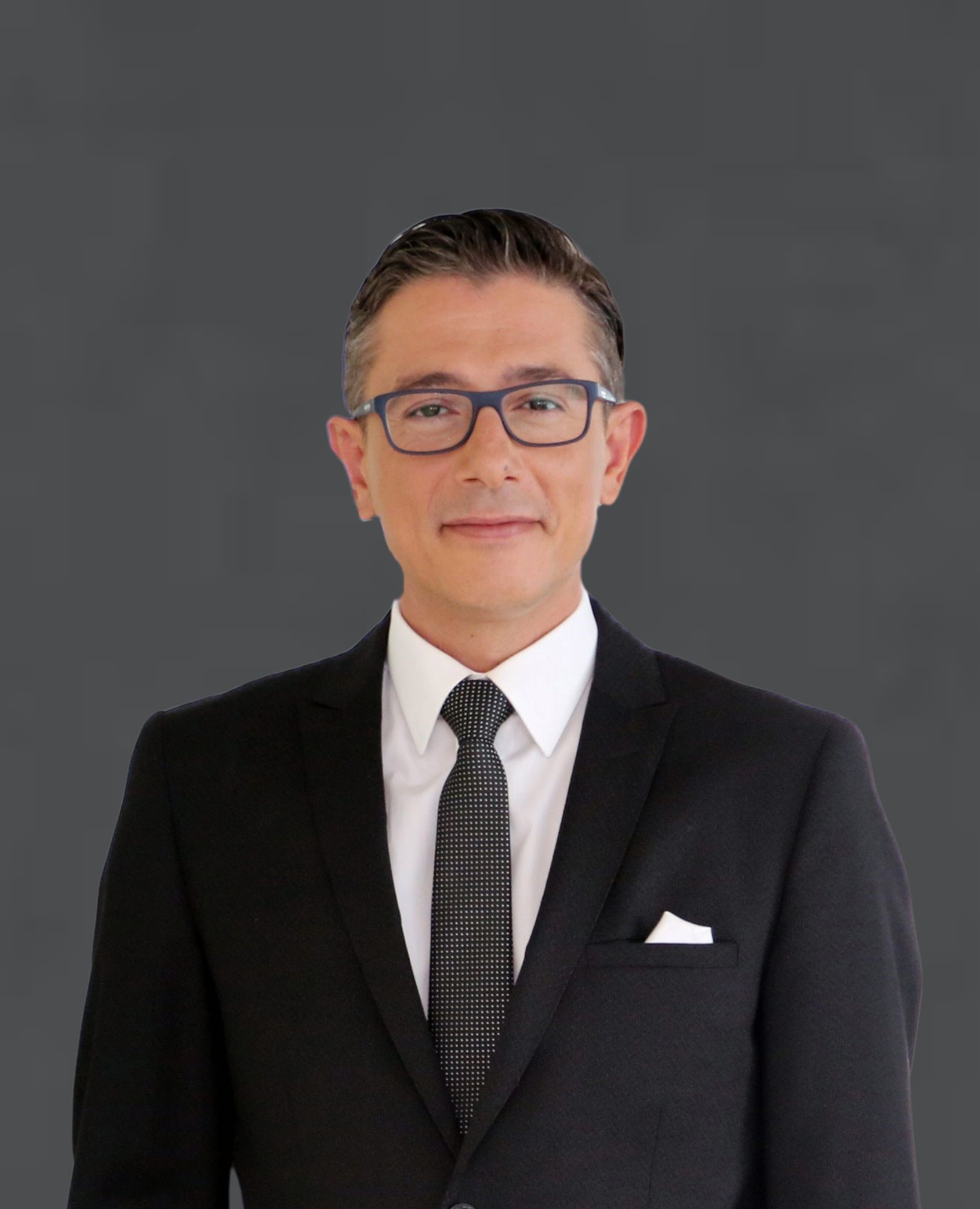 Porträt Okan Özdemir, Chief Officer Health von Allianz Partners. Mann mit kurzen, dunkelbraunen Haaren, schwarzer Brille, schwarzem Anzug, und grauer Krawatte.