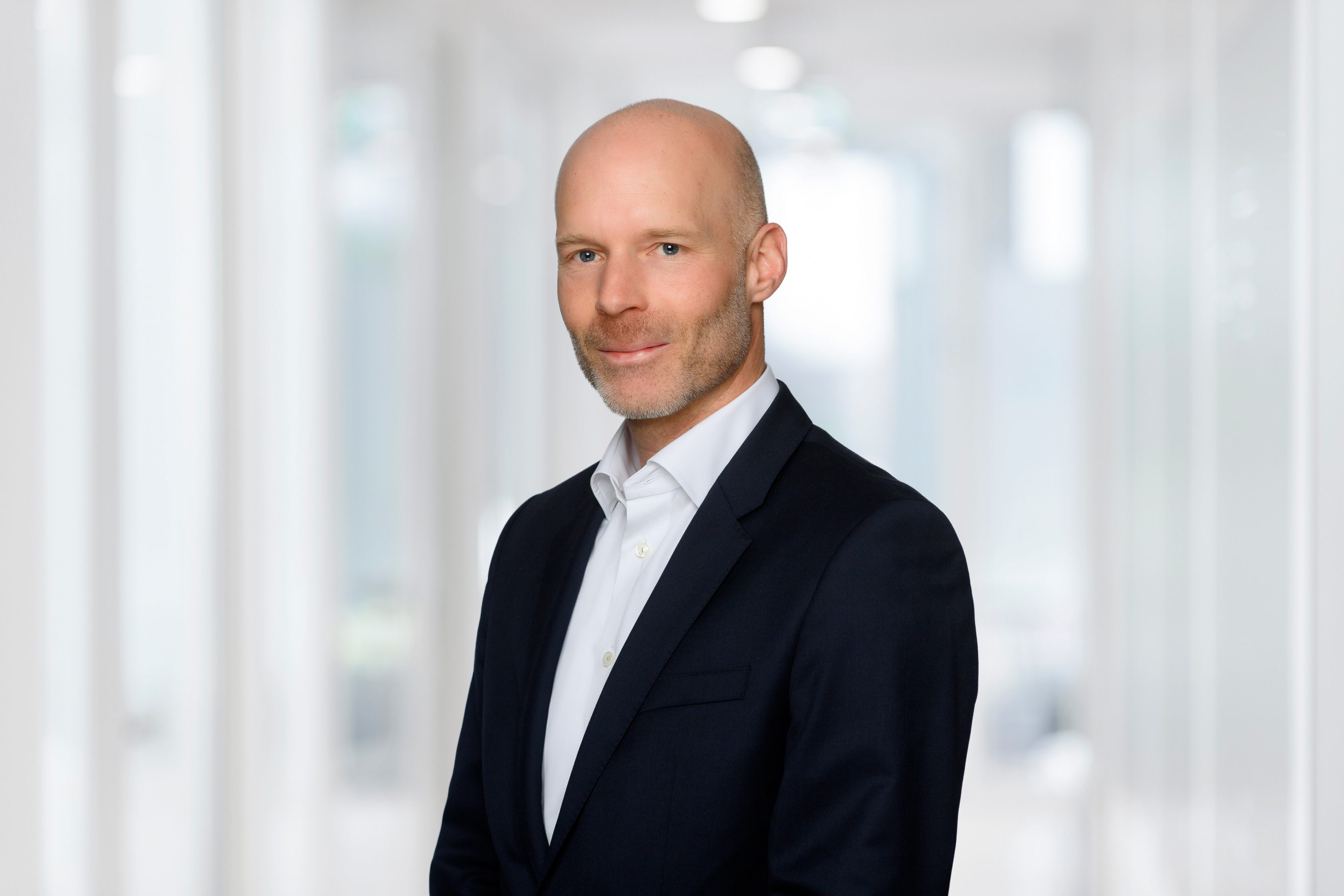 Das Bild zeigt Raphael Huegli, Finance Director bei Allianz Partners Deutschland. Er trägt einen Anzug mit weißem Hemd und lächelt ohne Zähne zu zeigen.