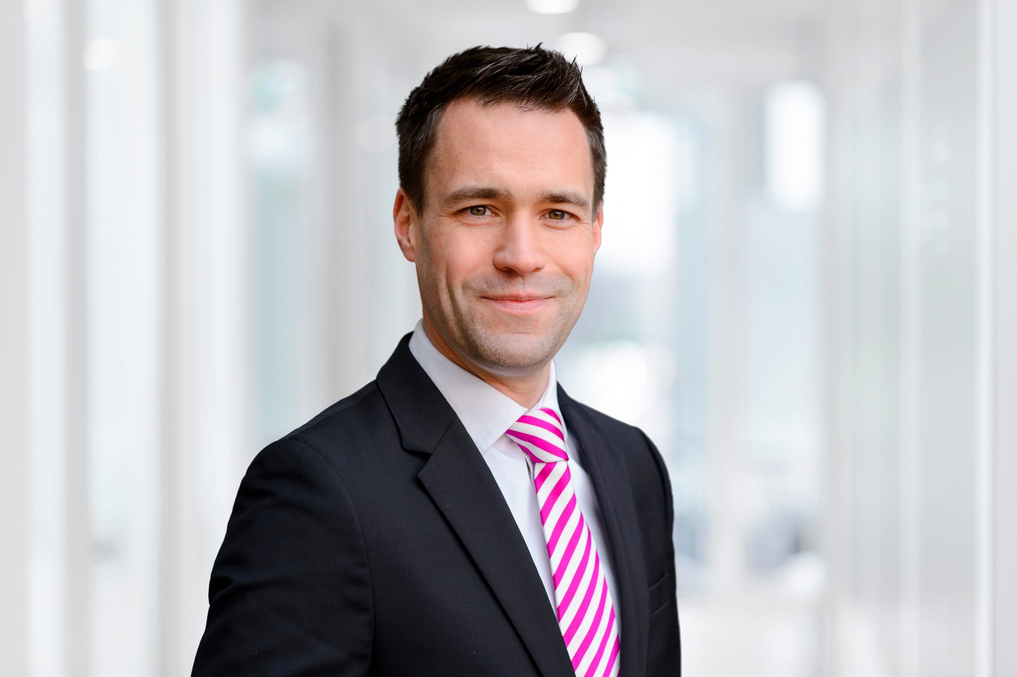 Das Bild zeigt Matthias Menke, Global Head of Home Operations Delivery. Er hat dunkle, kurze Haare, einen schwarzen Sakko, eine pink-weiß gestreifte Krawatte und lächelt.