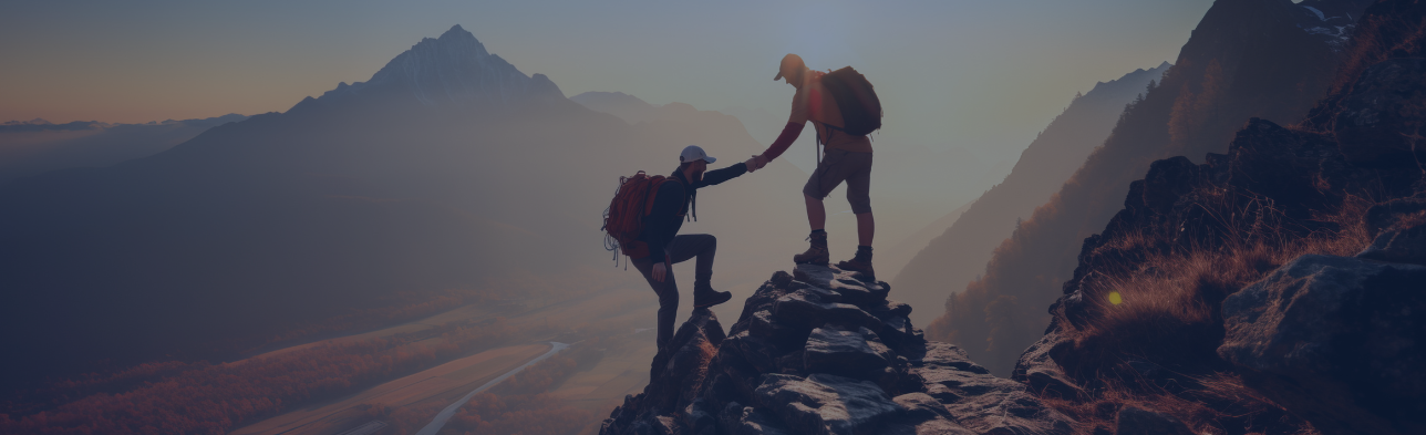 A hiker at the top of a mountain is helping another to the top.