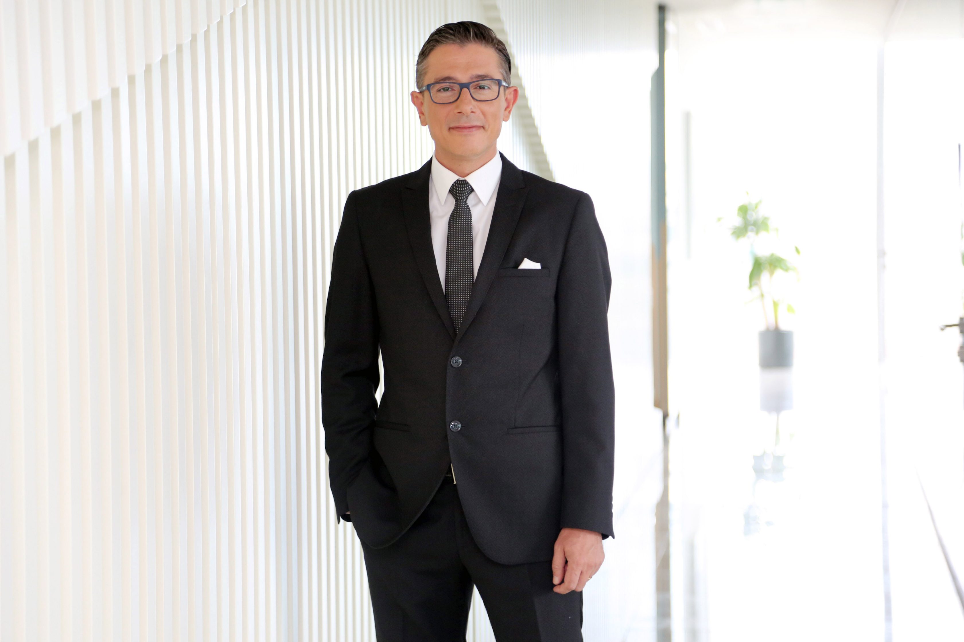 Okan Özdemir standing in a dark suit.