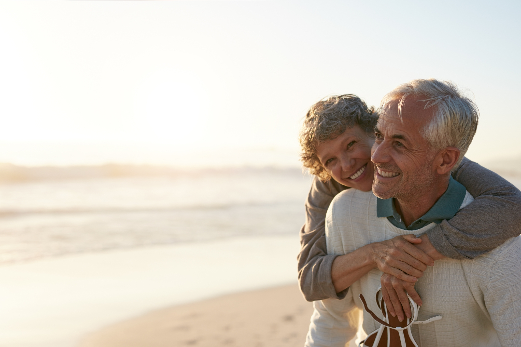 Elderly women draping her arms over an elderly man's shoulders in an embrace. Both people are smiling.