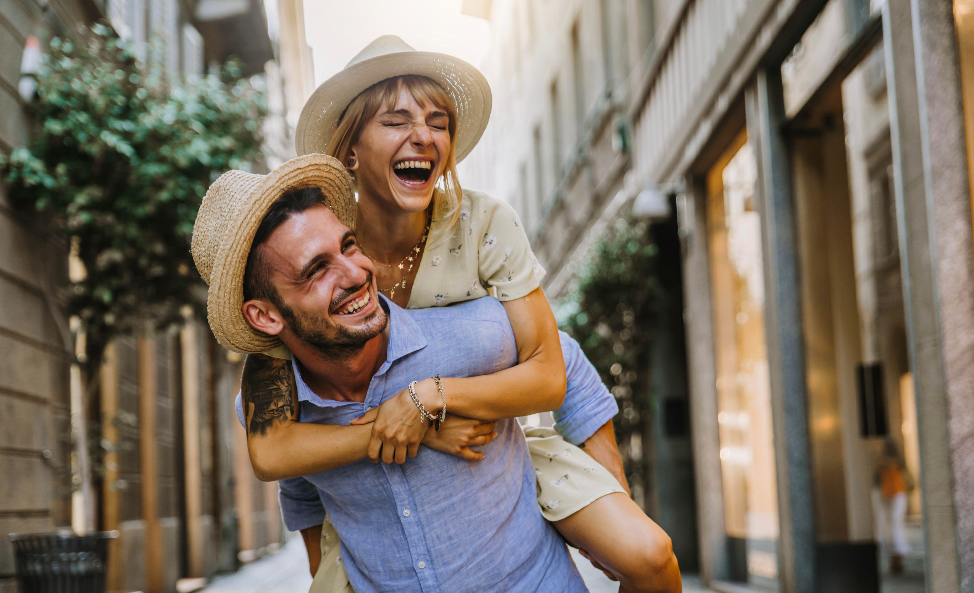 A man is piggybacking a woman in a European street, they are laughing.