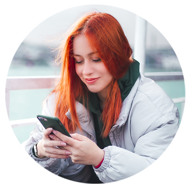 Eine junge Frau schaut auf Ihr Smartphone und lächelt.