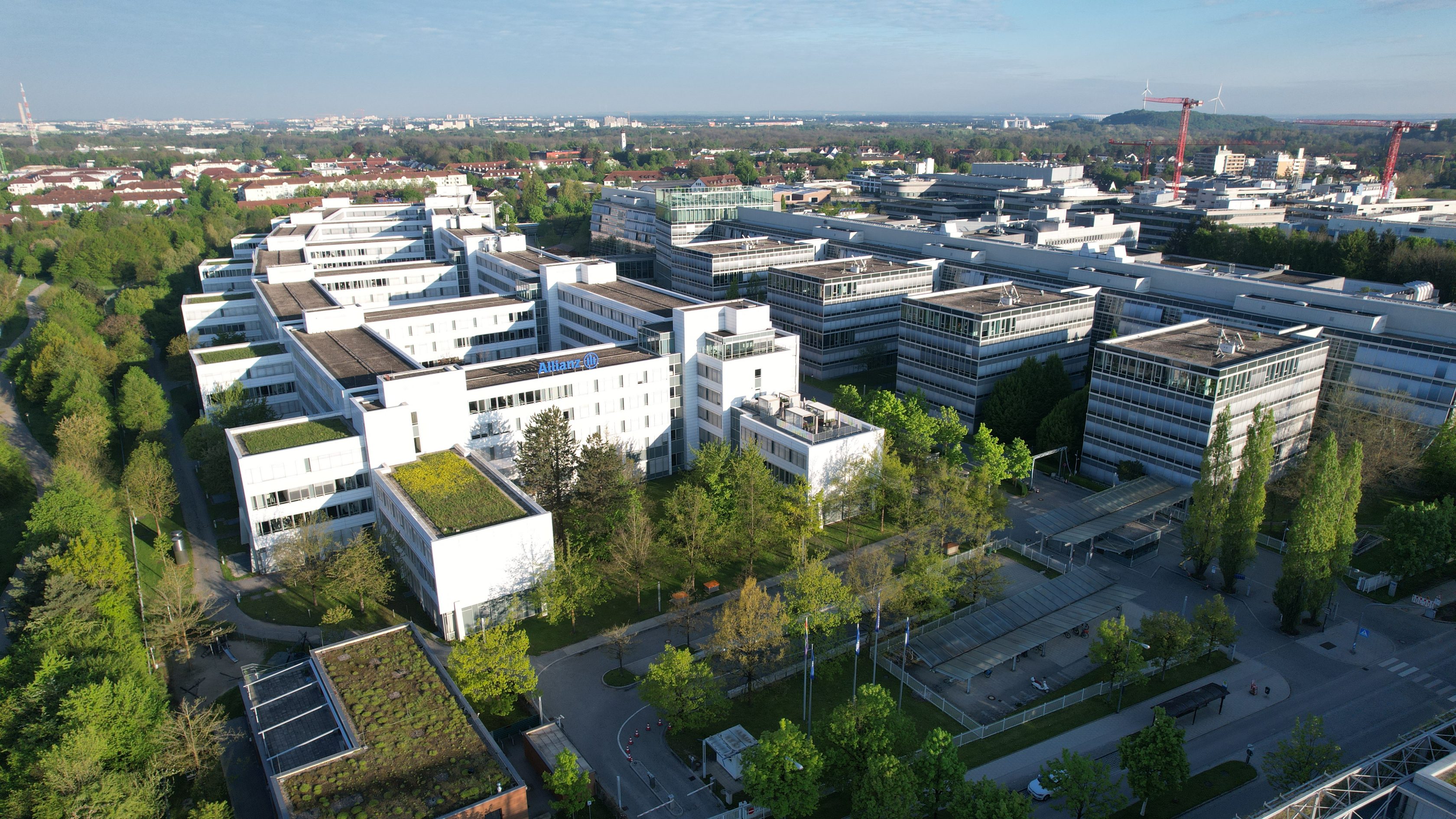 Allianz Campus in Unterföhring, Deutschland. Eine Luftaufnahme des weißen Bürogebäudes mit blauem Allianz Logo.