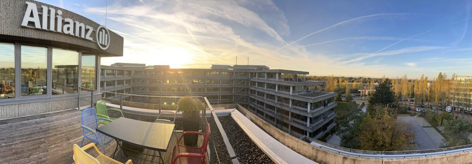 Standort Aschheim von Allianz Partners Deutschland. Ein Panoramabild von der Dachterasse und der Aussicht auf andere Gebäude und den Himmel bei Sonnenuntergang.
