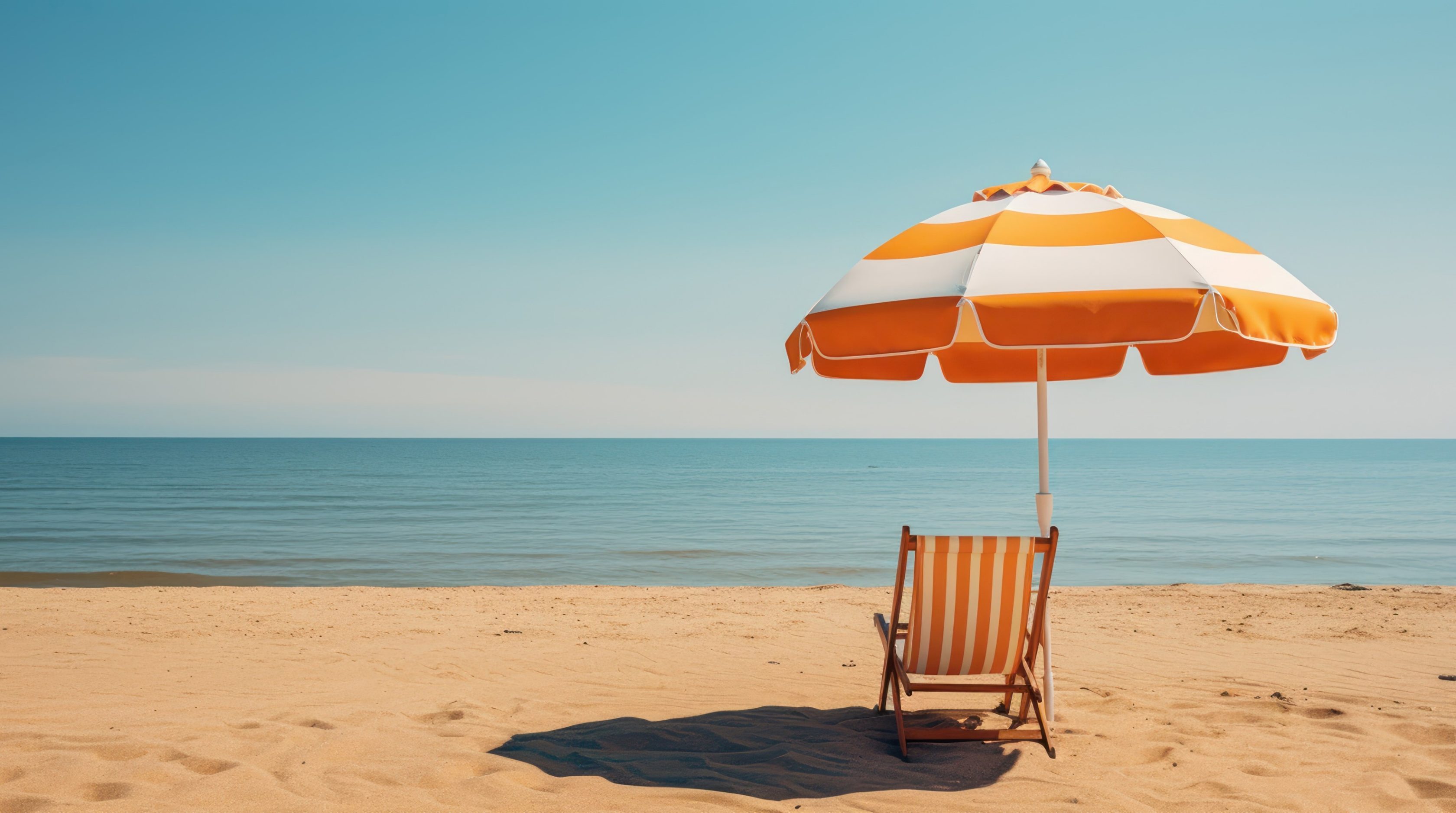 Ein orangener Liegestuhl und Sonnenschirm stehen am Sandstrand. Im Hintergrund ist das blaue Wasser und der Himmel zu sehen.