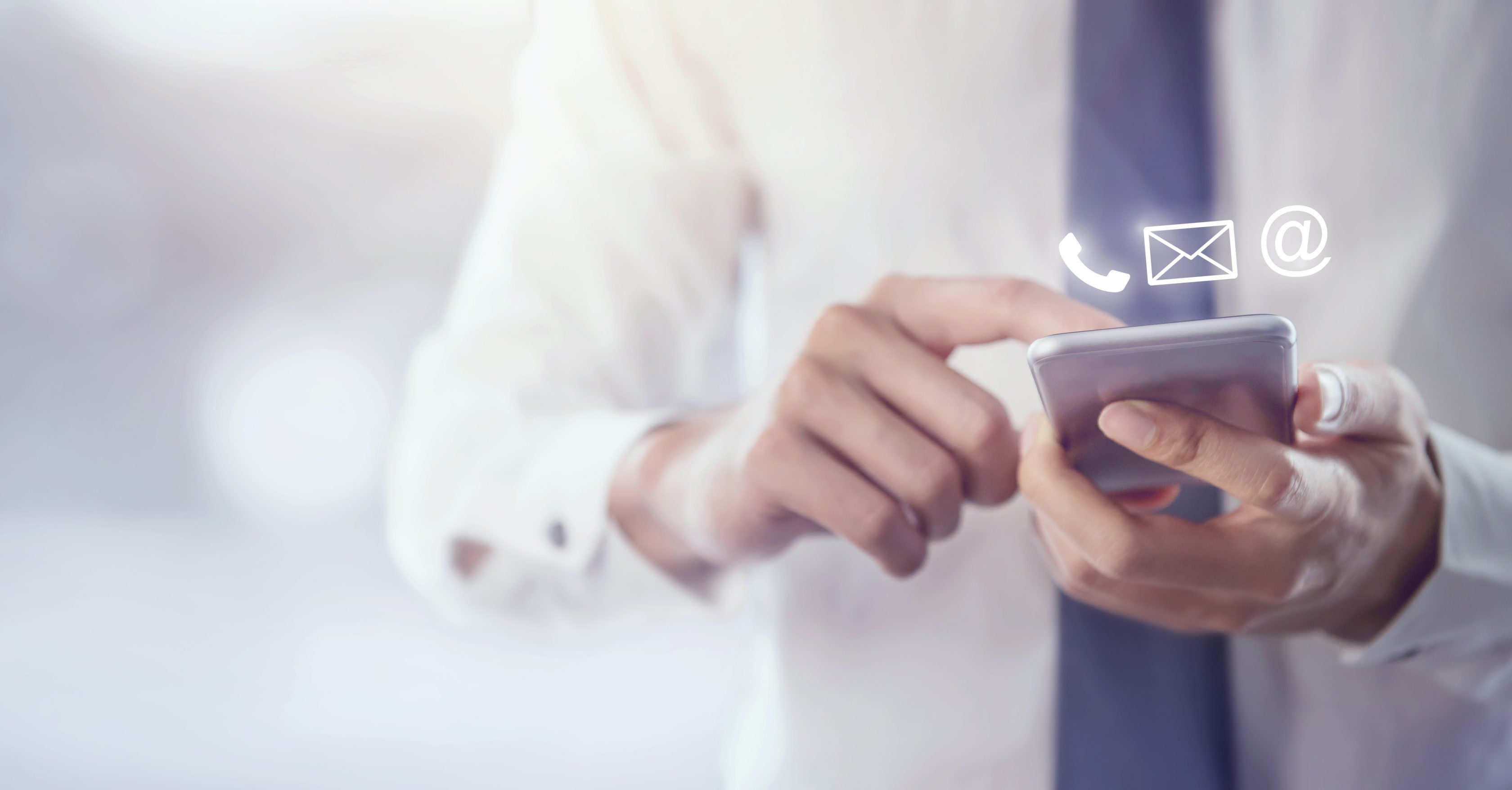 Ein Mann im hemd und mit Krawatte tippt auf ein Handy. Über dem handy schweben weiße Symbole von einem Telefonhörer, einem Brief und ein at-Zeichen.