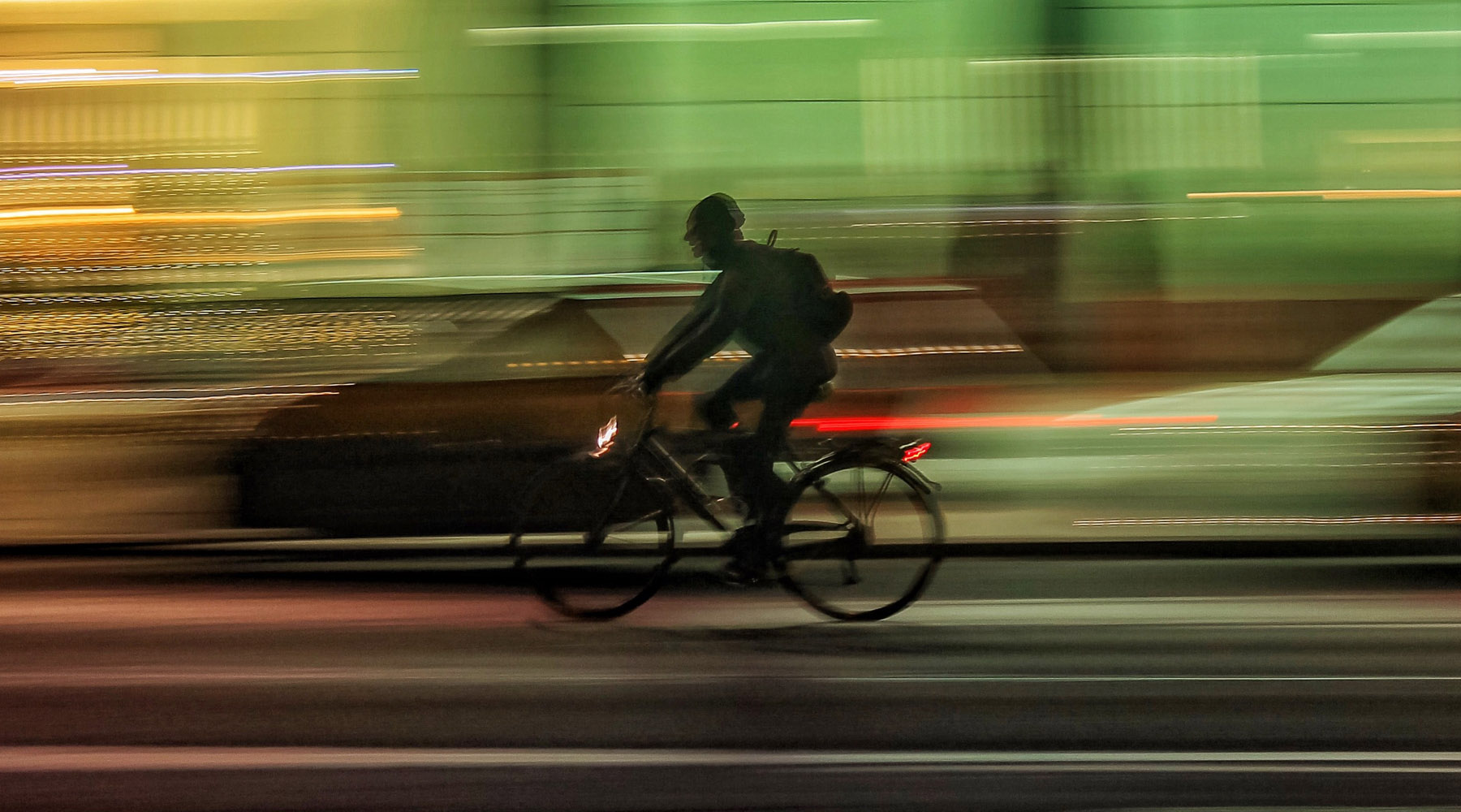 Ein Fahrradfahrer fährt auf einer Straße. Im Hintergrund sind verschwommen Autos zu erkennen.