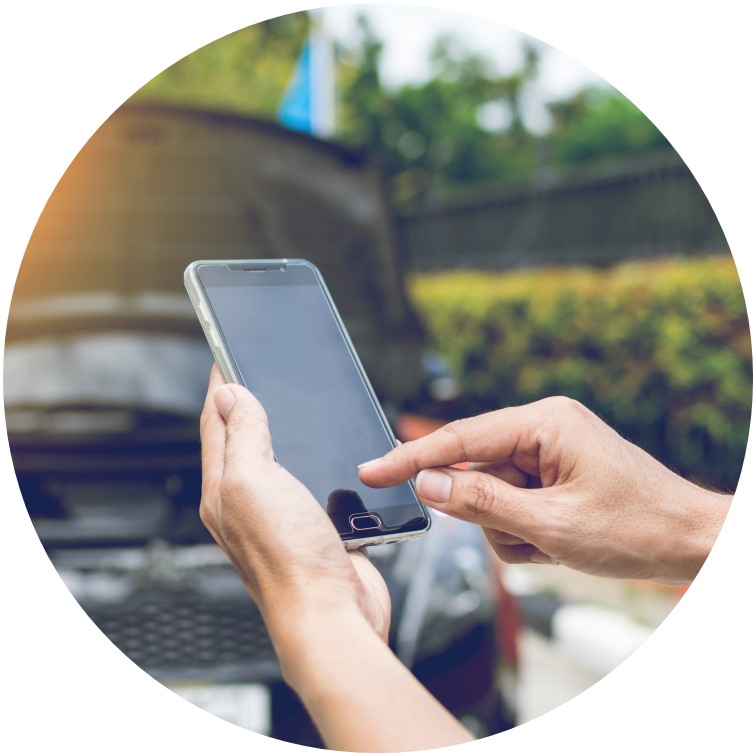 Ein runder Ausschnitt von einer Person, die auf ein Smartphone tippt. Im Hintergrund ist ein Auto mit geöffneter Motorhaube zu sehen.