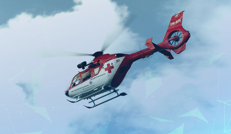 Im Hintergrund ist ein blauer Himmel mit Wolken zu sehen. Im Vordergrund sieht man einen weiß-roten Rettungshubschrauber mit rotem Kreuz.