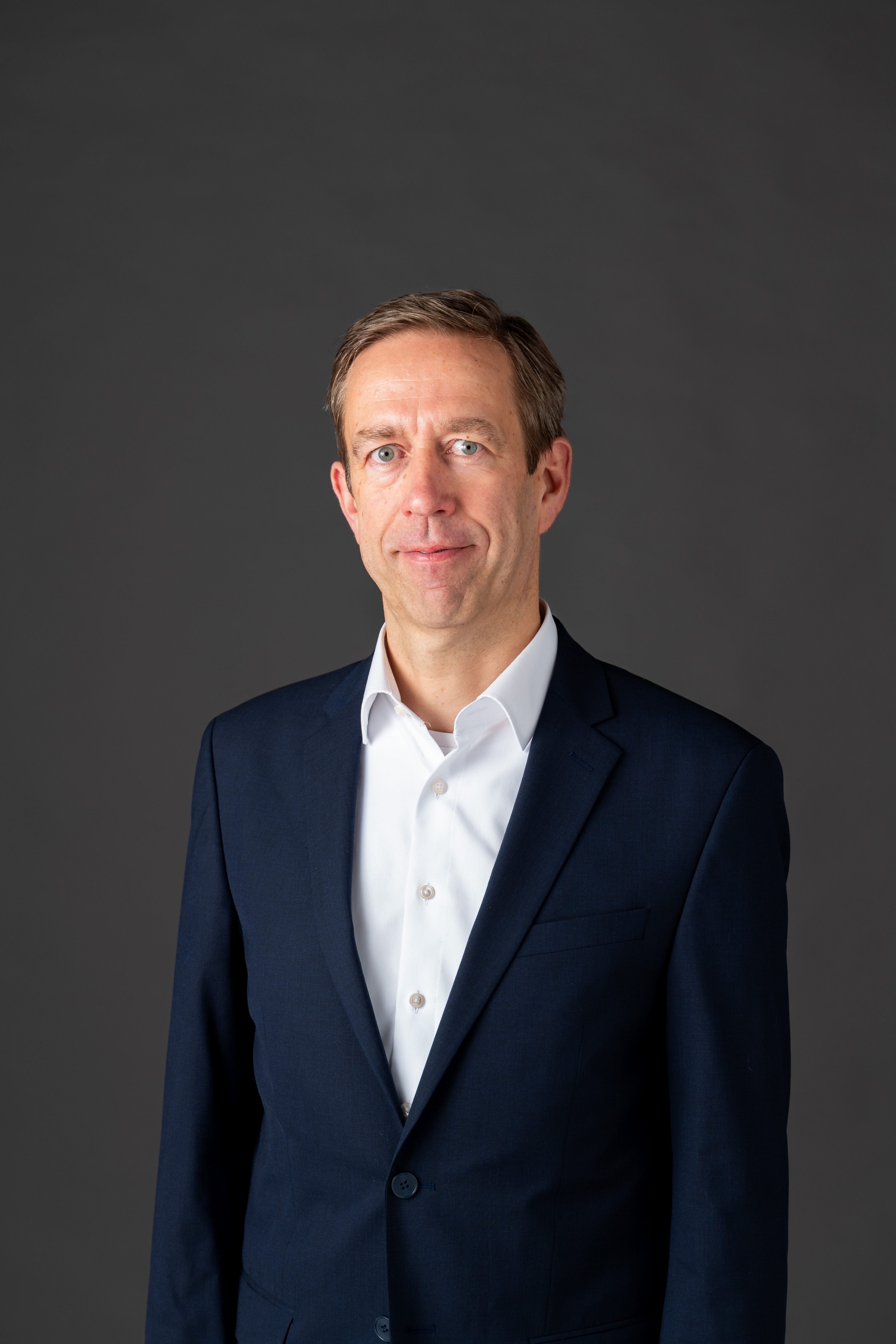 Michael Buttstedt ist Chief Financial Officer von Allianz Partners. Das Bild zeigt ihn vor einem grauen Hintergrund. Er trägt ein dunkelblaues Jackett und ein weißes Hemd.