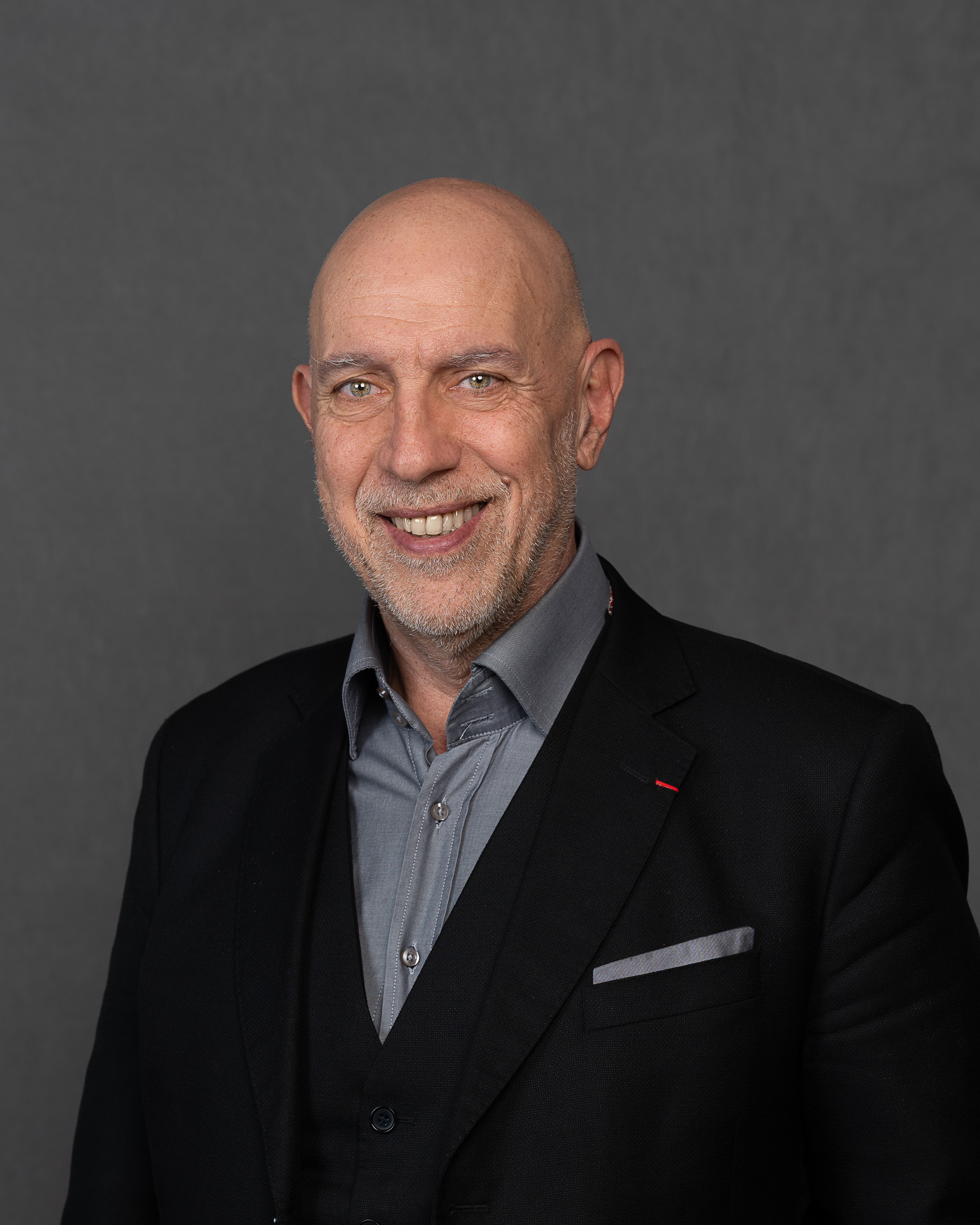Porträt von Jean-Marc Pailhol, Chief Officer Global Strategic Partnerships bei Allianz Partners. Mann mit Glatze und Bart, schwarzes Sakko, graues Einstecktuch und Hemd